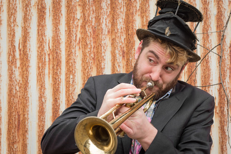 Stylish bearded gypsy plays trumpet by rusty fenceの写真素材