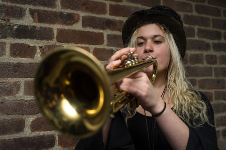 Stylish blonde gypsy girl plays trumpet by brick wallの写真素材