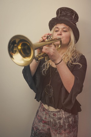 Stylish blonde gypsy girl wears top hat and plays trumpetの写真素材
