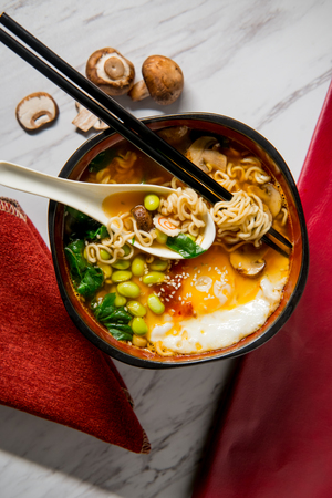 Spicy edamame and narutomaki spiral ramen noodle soup with runny fried eggの写真素材