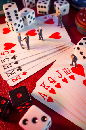 Miniature businessmen figurines making a deal on casino gambling card game table