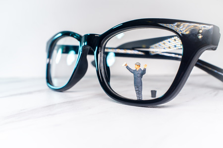 Optician eyeglasses being cleaned by tiny figurine symbolizing clear visionの写真素材
