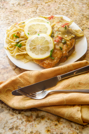 Italian chicken piccata schnitzel with artichoke hearts served on fettuccineの写真素材