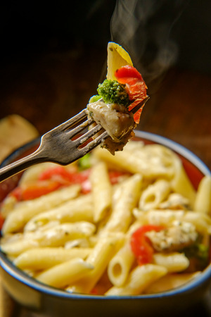 Grilled chicken alfredo penne primavera with dark moody lighting on rustic wooden kitchen tableの写真素材