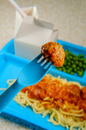 Grade school lunch tray of Italian spaghetti and meatballs with green peas milk carton and jellyの写真素材