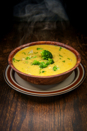 Rustic hearty broccoli and cheddar cheese soup on wooden kitchen tableの写真素材