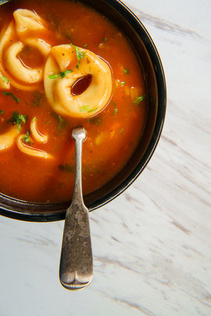 Fresh hot tortellini tomato soup on marble kitchen tableの写真素材