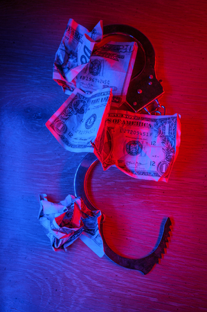 Conceptual handcuffs with crumpled dollar bills and police lightsの写真素材