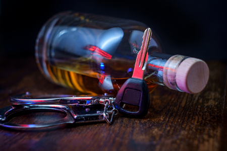 Half empty bottle of whisky on rustic wooden bar with keys and handcuffs symbolizing drunk driving arrestの写真素材