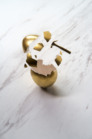 Tiny hammer breaks golden egg with shattered shell pieces actionの写真素材