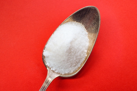 Spoonful of sugar on red background diabetes and blood sugar conceptの写真素材