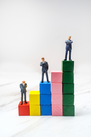 Miniature businessmen stand on wooden blocks symbolizing steps to success