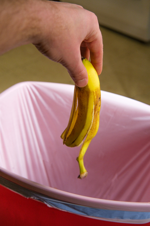 Throwing away old banana peel in red garbage canの写真素材