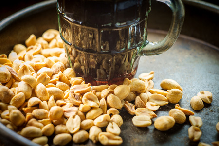 Frothy beer shelled salty pub peanuts on wooden bar tableの写真素材