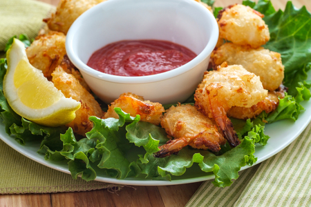 Breaded and fried butterfly coconut shrimp served on bed of romaine lettuce with spicy cocktail dipping sauceの写真素材