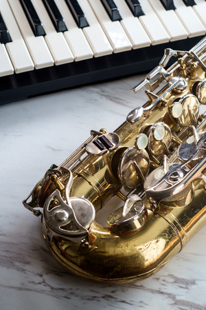 Rusty old classical saxophone on marble table next to electric piano keyboardの写真素材