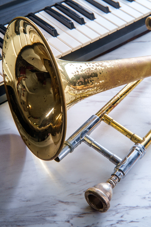Rusty old classical trombone on marble table next to electric piano keyboardの写真素材