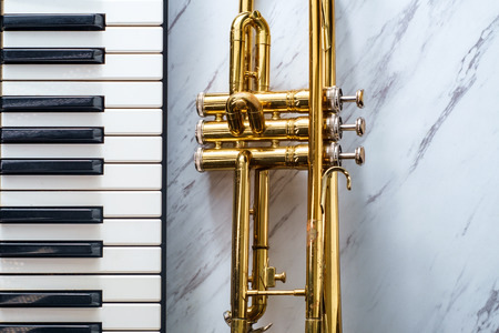 Rusty old classical trumpet on marble table next to electric piano keyboard