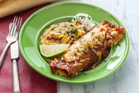 Authentic Mexican chimichanga enchilada with sour cream and rice garnished with lime wedgeの写真素材