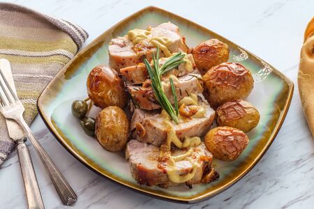 Sliced honey mustard roast pork tenderloin with baby potatoes and caperberry garnishの写真素材
