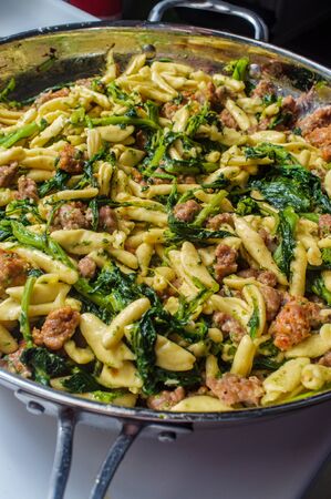 Italian spicy sausage ricotta cavatelli pasta and broccoli rabe simmering on kitchen stoveの写真素材