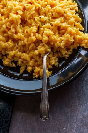 Delicious spiral macaroni and cheddar cheese on black plateの写真素材