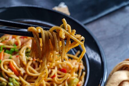 Eating Chinese chicken chow mein noodles with chopsticks