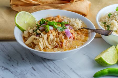 White navy bean chicken chili with tortilla strips lime cilantro and shredded cheese garnishの写真素材