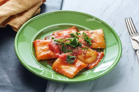 Italian ravioli with tomato marinara sauce topped with chopped parsley and grated parmesan cheeseの写真素材