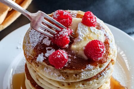 Pancakes with maple syrup powdered sugar raspberries and butterの写真素材