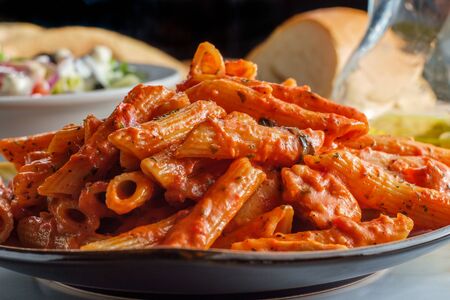 Italian penne pasta in creamy vodka tomato sauce with grilled chicken on marble kitchen tableの写真素材