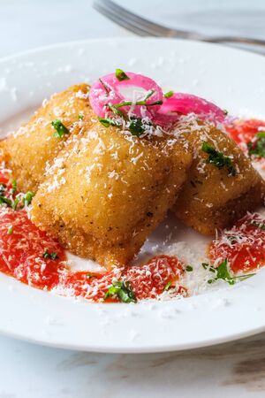 Breaded fried Italian ravioli topped with pickled red onions and grated pecorino romano cheese and hot marinara tomato sauceの写真素材