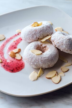 Powdered sugar cake doughnuts with holes served with raspberry jam and slivered almondsの写真素材
