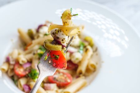 Gluten free Italian pesto pasta salad with pearl mozzarella cheese balls and halved cherry tomatoesの写真素材