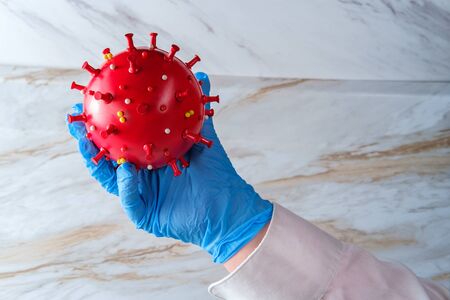 Scientist holding deadly epidemic coronavirus cell closeup concept with protective rubber glovesの写真素材