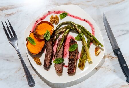 Well done sliced beef rib boneless club steak with parmesan garlic asparagus and baked sweet potatoes plated with raspberry walnut の写真素材