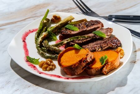 Well done sliced beef rib boneless club steak with parmesan garlic asparagus and baked sweet potatoes plated with raspberry walnut の写真素材