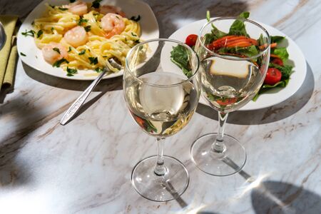 Romantic Italian dinner with two glasses of pinot grigio white wine and fettuccine alfredo shrimp in the backgroundの写真素材