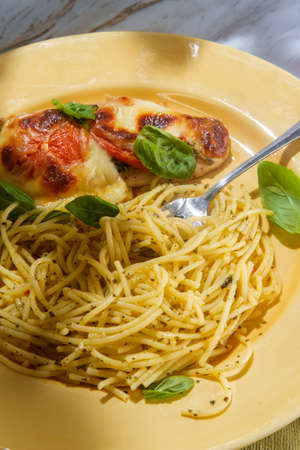 Mozzarella baked caprese chicken breast with pesto spaghetti and basil garnishの写真素材