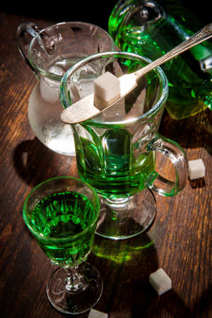 Green absinthe liquor in glass with ice water to pour over sugar cube
