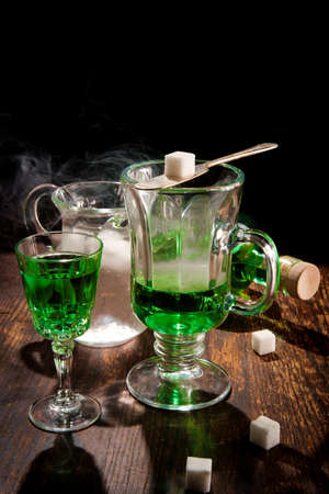 Green absinthe liquor in glass with ice water to pour over sugar cube