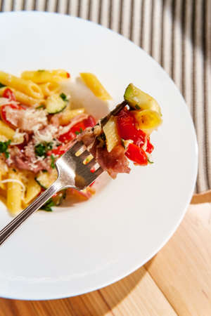 Gourmet Italian penne pasta with tomatoes zucchini and prosciutto garnished with grated asiago cheese and parsleyの写真素材