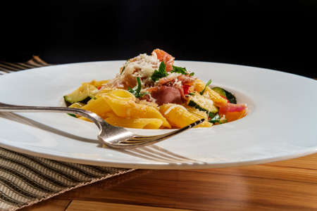 Gourmet Italian penne pasta with tomatoes zucchini and prosciutto garnished with grated asiago cheese and parsleyの写真素材