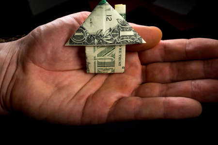 Hand holds origami paper money house for real estate and housing market conceptの写真素材