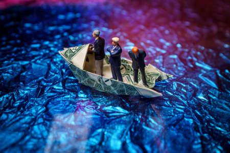 Miniature figurine businessmen ride on dollar bill origami yachtの写真素材