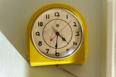Old dirty antique yellow electric clock hanging on wall