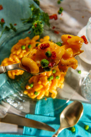 Macaroni and cheese with green peas and crushed red pepper on bright sunny day