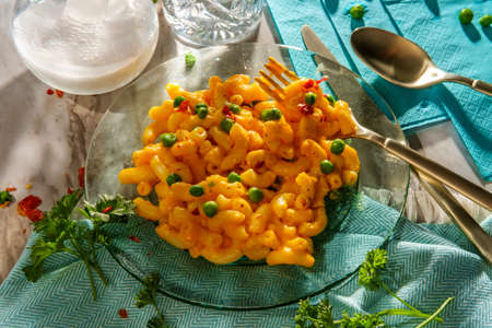 Macaroni and cheese with green peas and crushed red pepper on bright sunny day