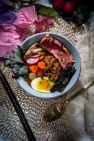 Seared pink ahi tuna ramen garnished with soft boiled egg seaweed strips radish and multicolored sliced carrotsの写真素材