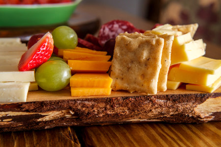 Italian charcuterie board featuring crackers cheese and salami served on wooden plank with raw bark...